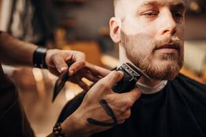 Fotografi Male barber cutting beard of client in barber shop, South_agency