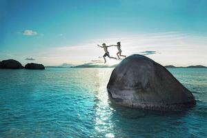 Fotografi Two kids holding hands jumping off rock into sea, Gary John Norman, (40 x 26.7 cm)