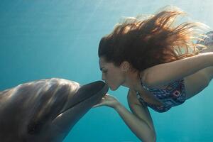 Fotografi Young Woman Kisses Dolphin Underwater, Sunbeams, Justin Lewis, (40 x 26.7 cm)