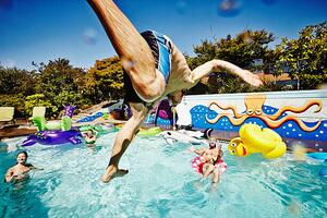 Fotografi Man in mid air jumping into pool during party, Thomas Barwick, (40 x 26.7 cm)