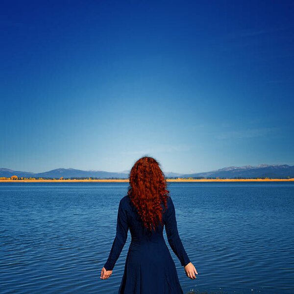 Konstfotografering Redhead in blue dress faces rippled lake, Anna Gorin, (40 x 40 cm)
